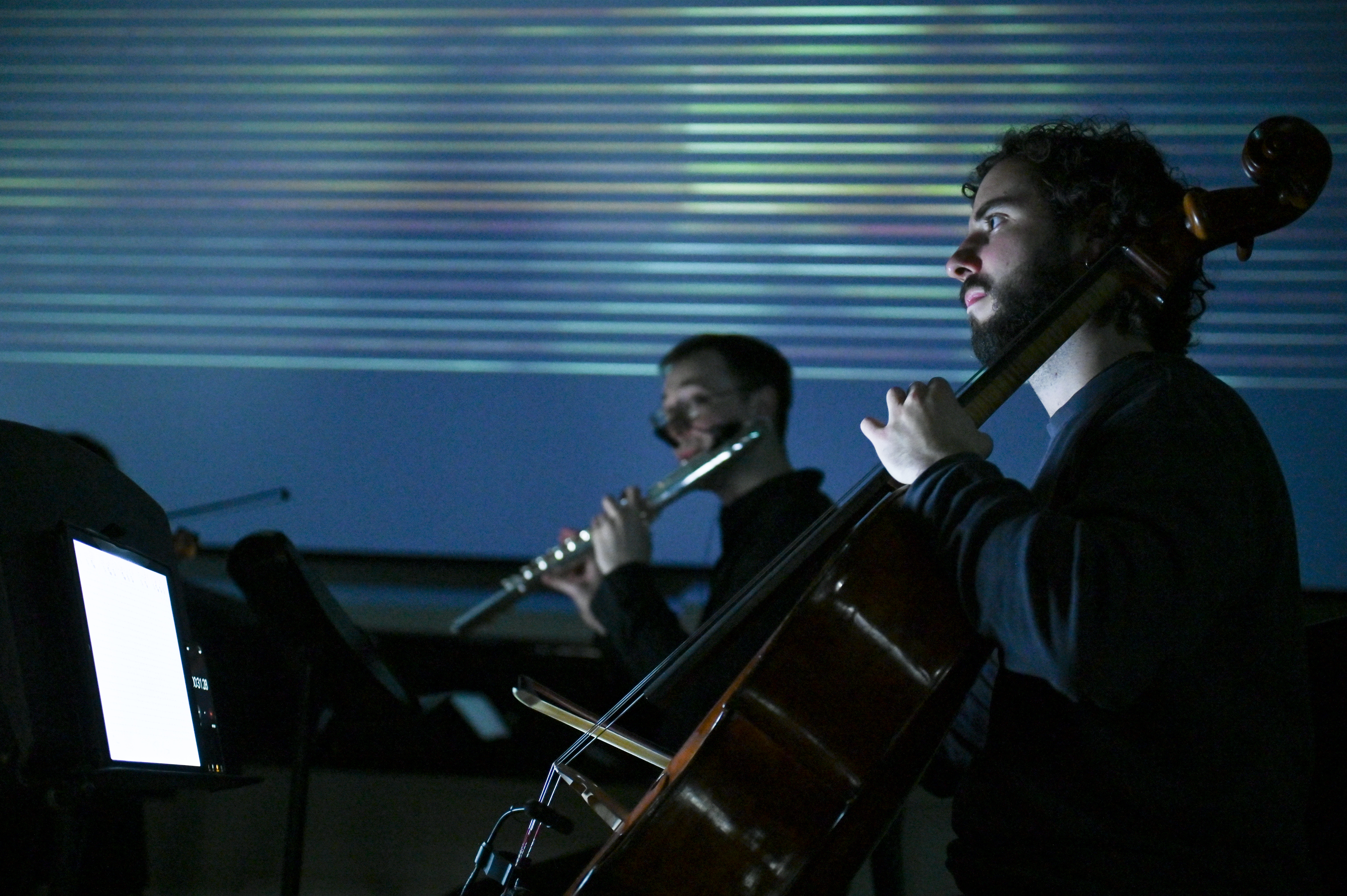 A cellist and a flautist performing against a dark blue background
