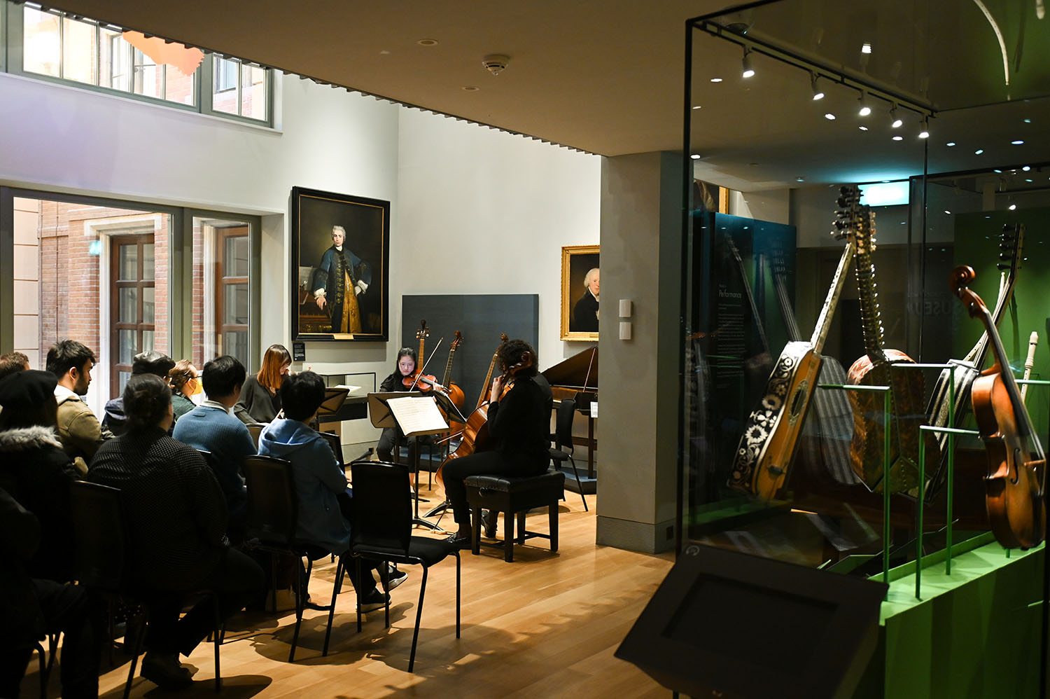 A string quartet performs in the RCM Museum to a full audience with the display cases of guitars on show to the right