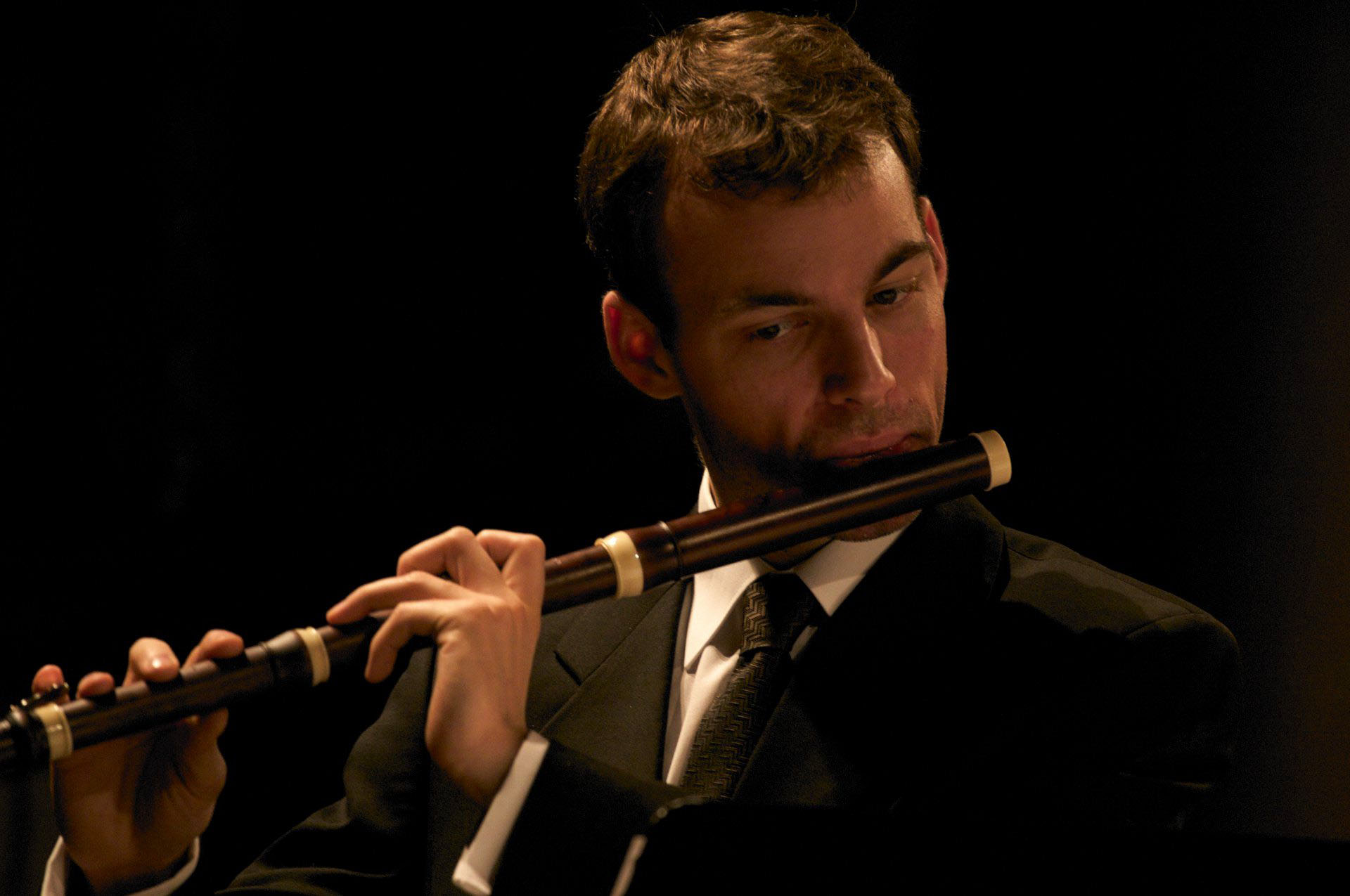 A man wearing black performing on a baroque flute