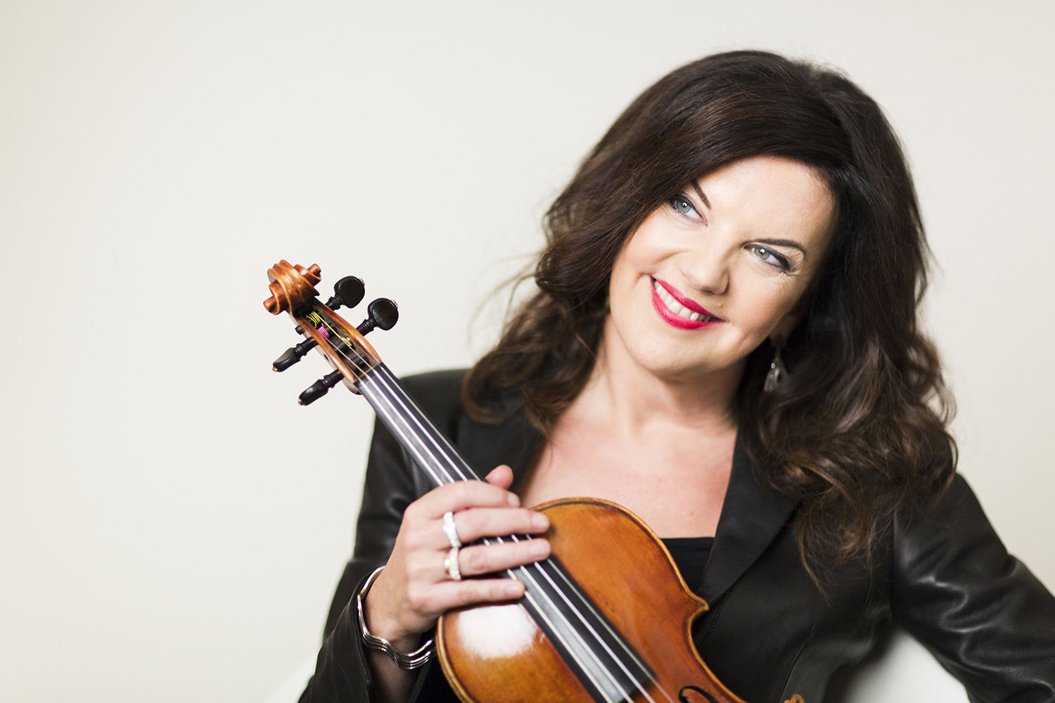 A woman with dark hair wearing black and holding a violin, smiling looking off to the side