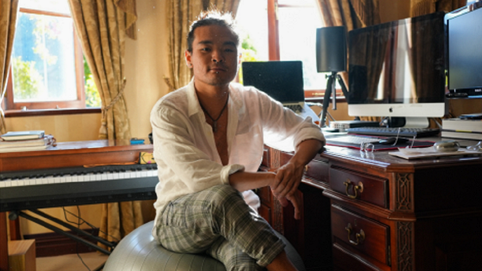 Photo of male alumnus sitting at a piano with his legs crossed.