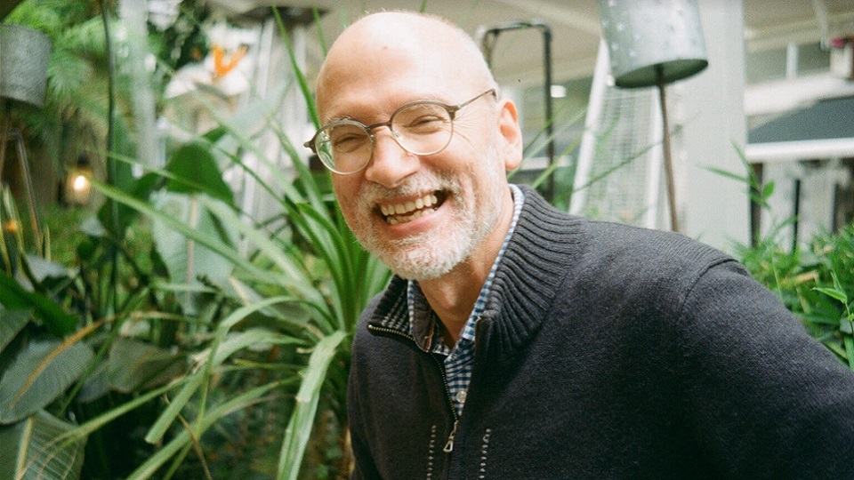 A man wearing glasses and a dark jumper, smiling at the camera.