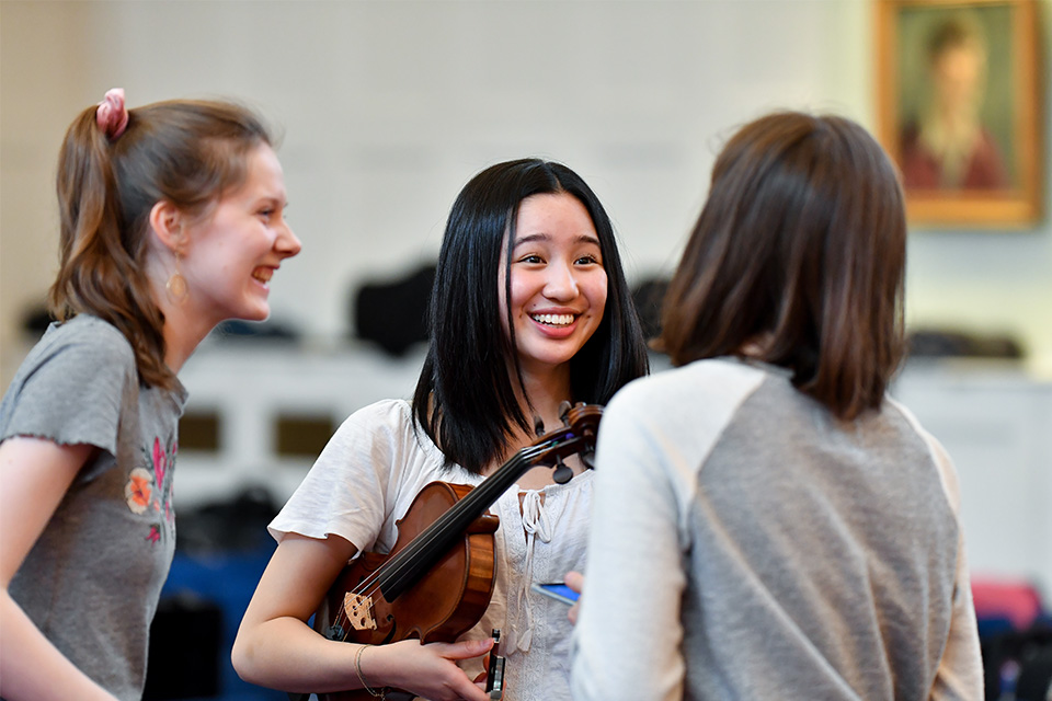 Three Junior Department students standing holding instruments and smiling