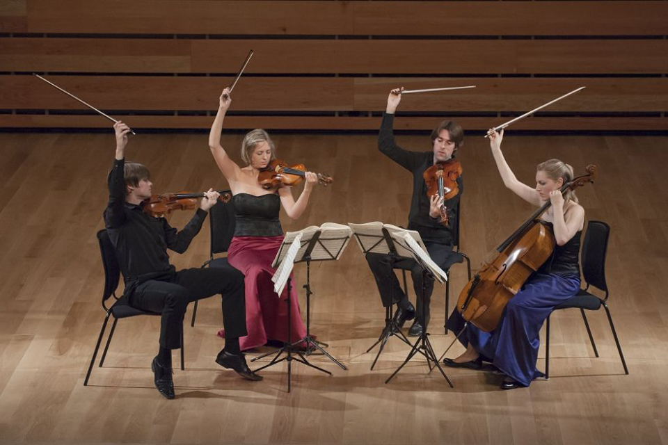 The Sacconi Quartet lifting their bows into the air during a performance