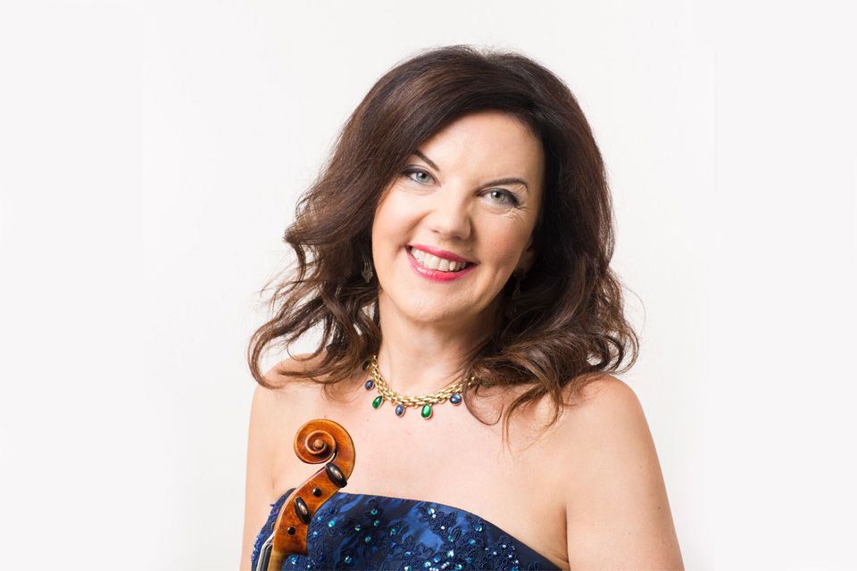 Tasmin Little holds her violin and smiles against a white background