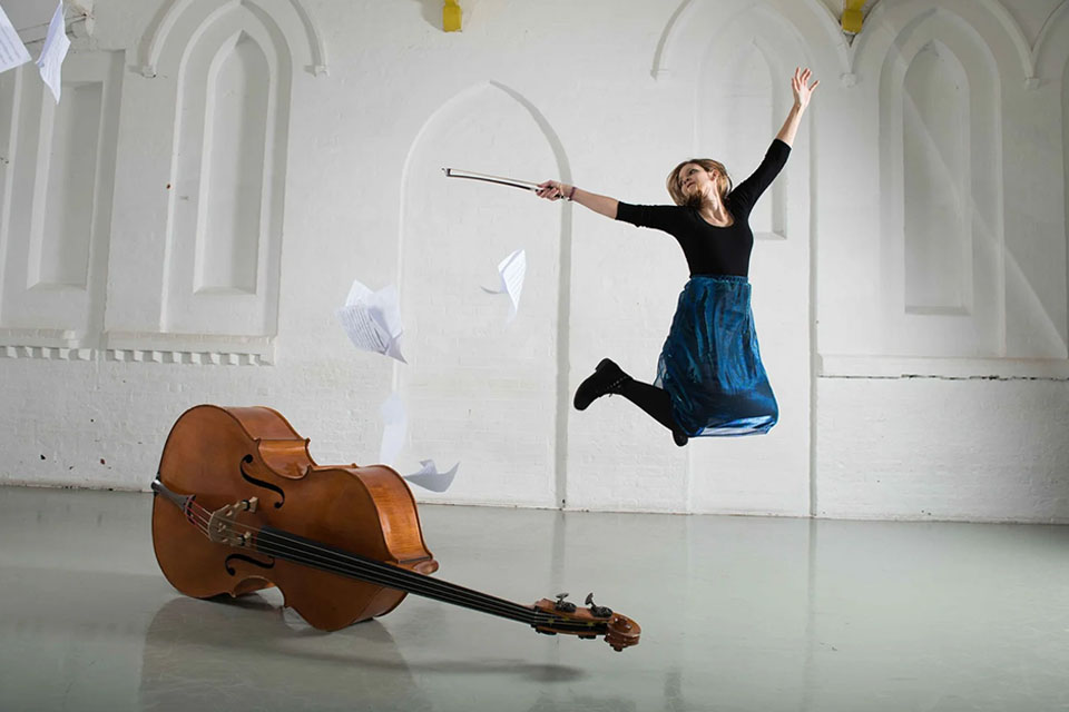 Valentina Scheldhofen Ciardelli jumps in a white studio with a double bass to the left hand side