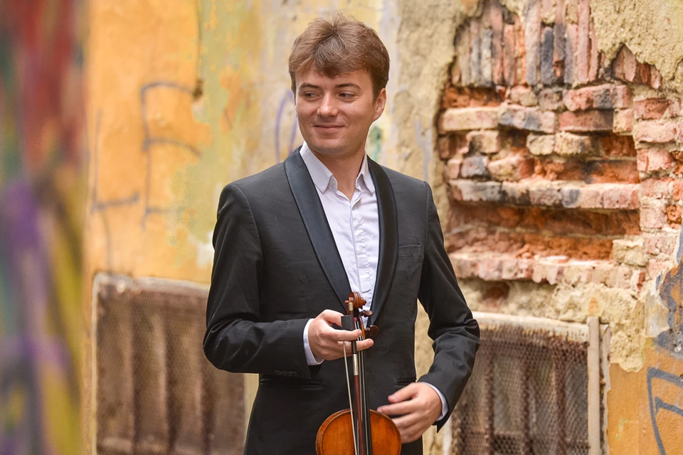Vlad Maistorovici holding his violin, standing in front of a graffitied wall