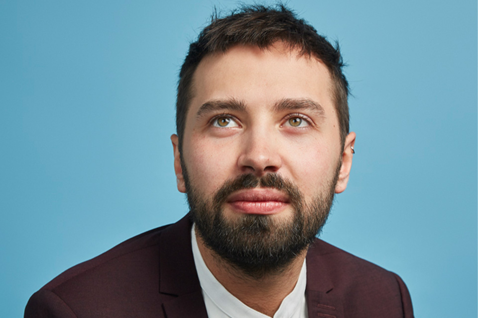 Adam Walker, wearing a mauve jacket, looks upwards against a light blue background