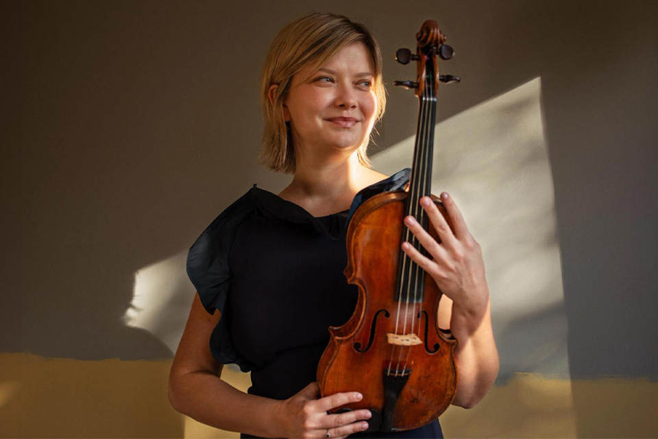 Alina Ibragimova Holds her violin and smiles in a sunlit room