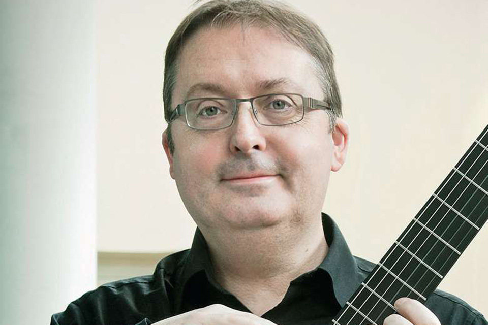 A headshot of Guitarist Allan Neave holding his instrument, taken in front of a light background