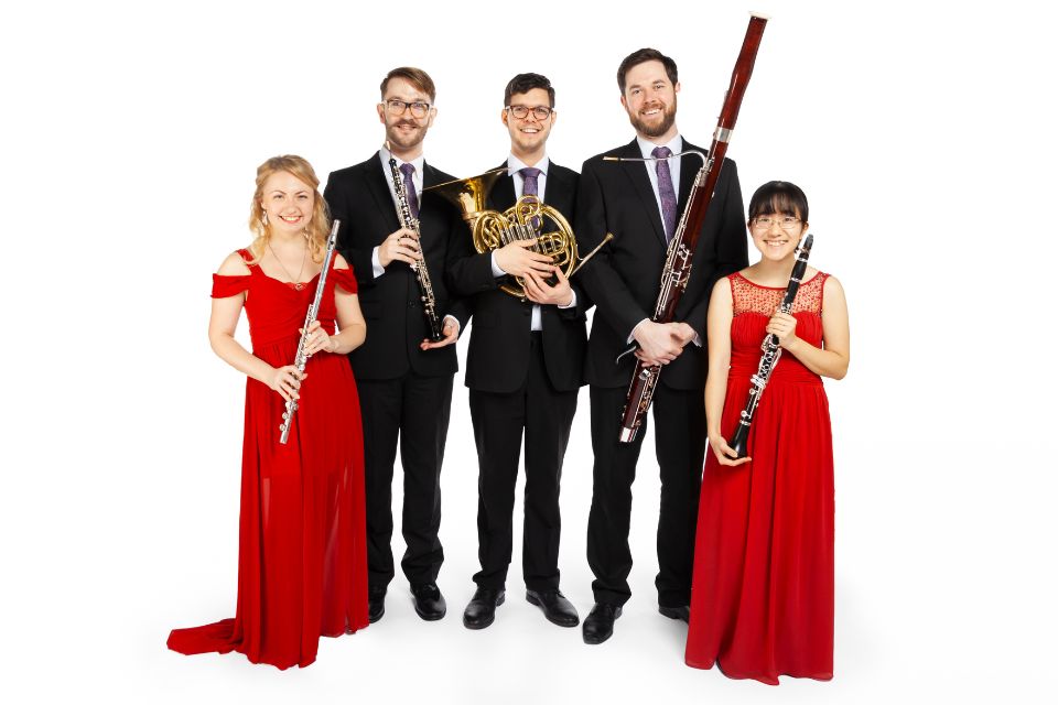 A group of people stand in a white room holding musical instruments