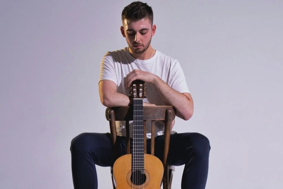 A young man sits holding a guitar