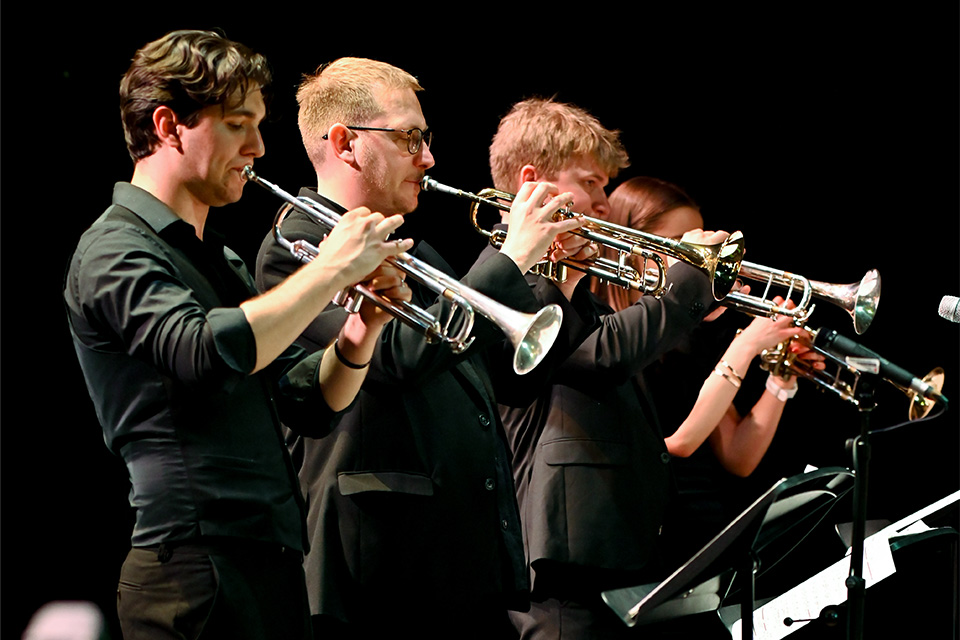 Three young men in black shirts play trumpets on stage