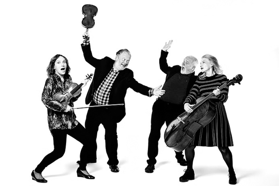 A black and white photo of four musicians holding their instruments in the air excitedly
