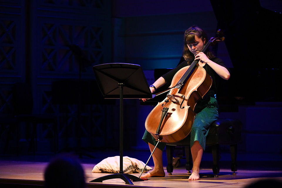A cellist performs on stage under colourful lights