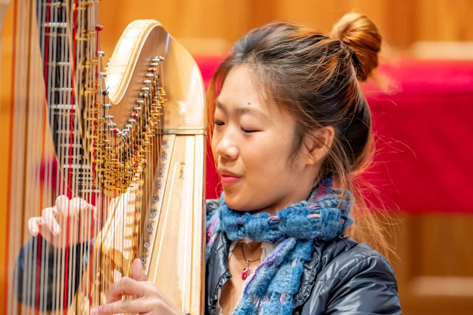 A young woman wears a blue scarf and plays the harp