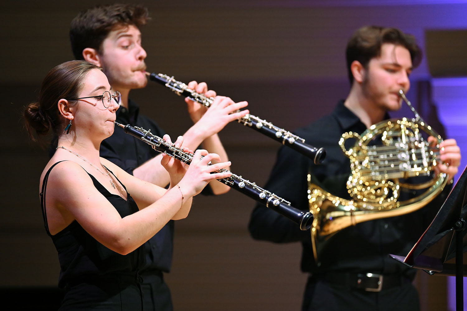 Two oboeists perform and a hornist perform on stage