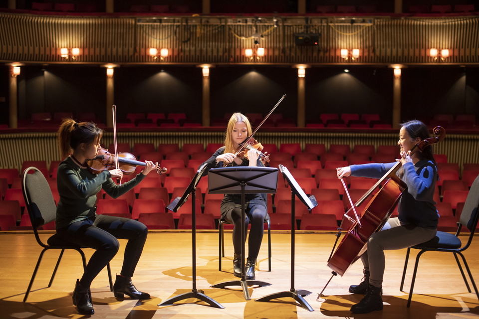 A trio of RCM string players perform, with the Britten Theatre auditorium visible behind them