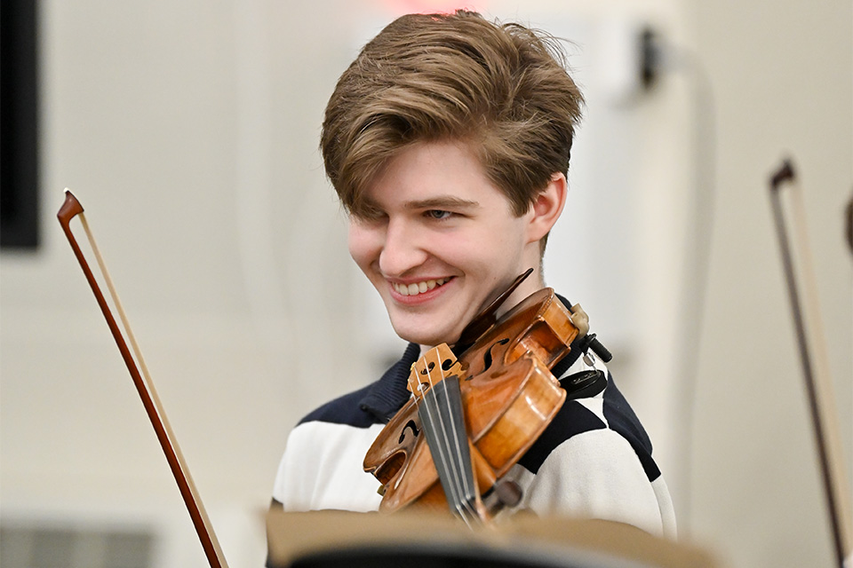 A young man smiles while playing the violin