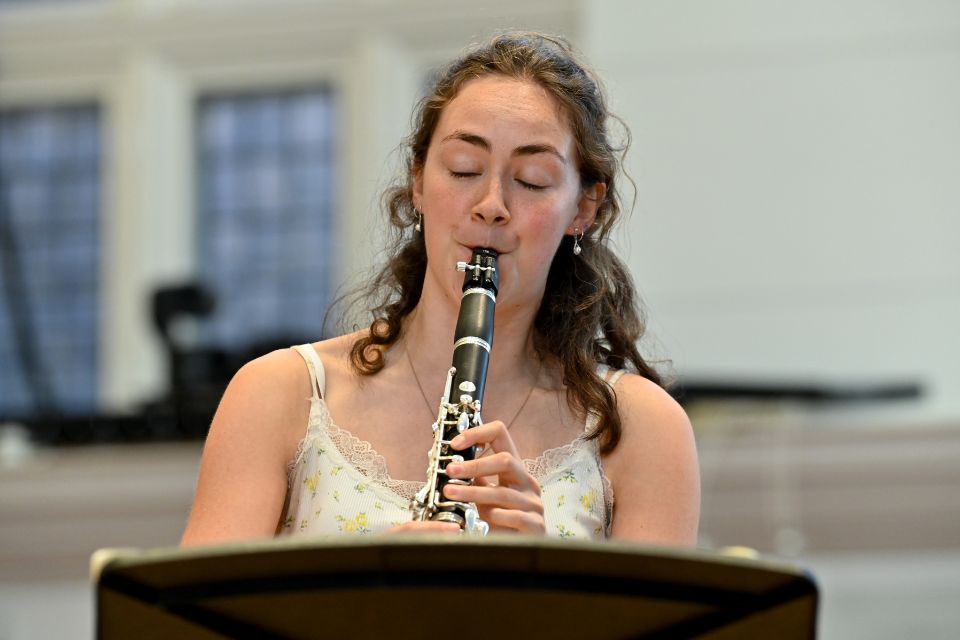 A young woman plays the clarinet in a bright room