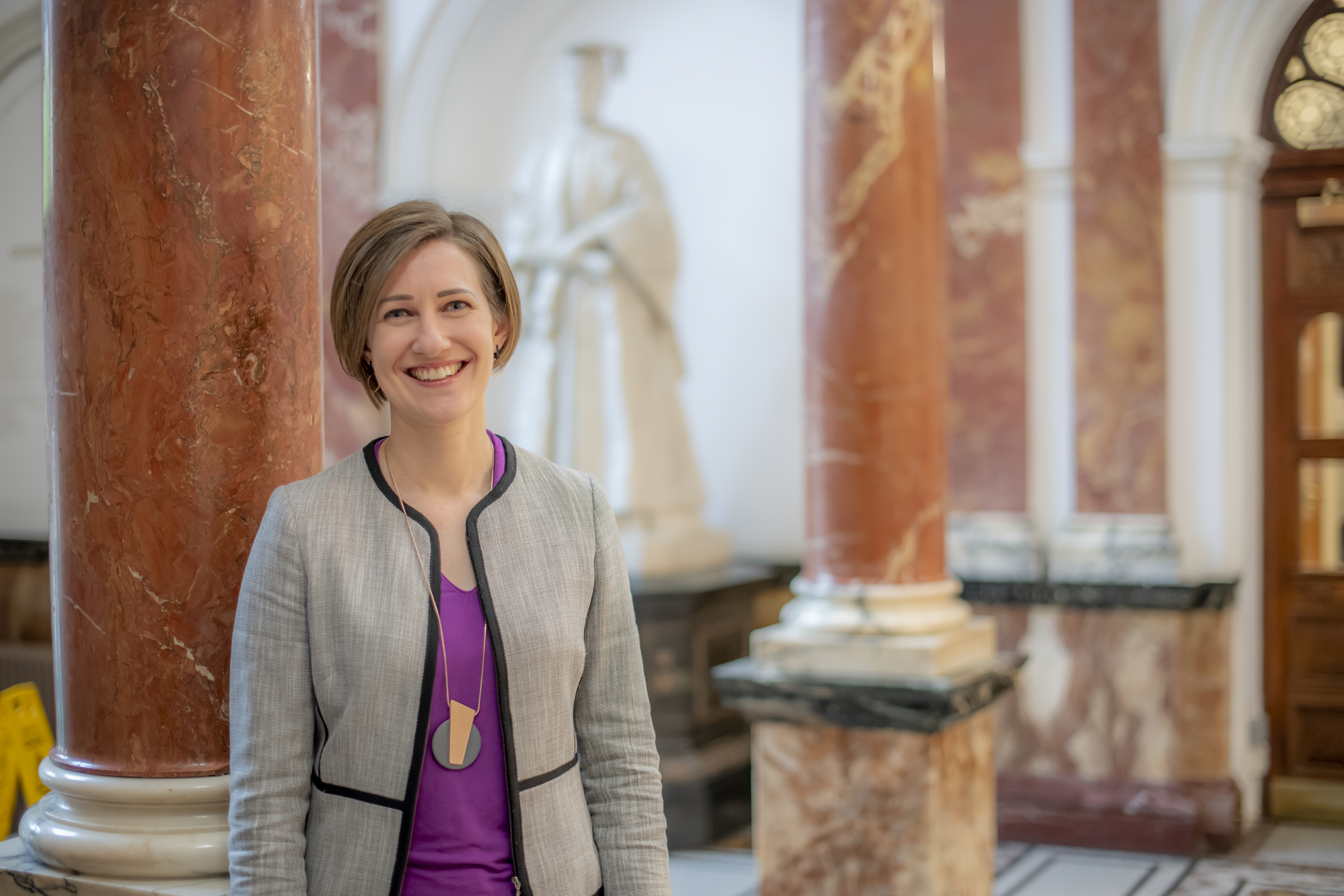 A woman with short brown hair standing in the RCM foyer smiling at the camera