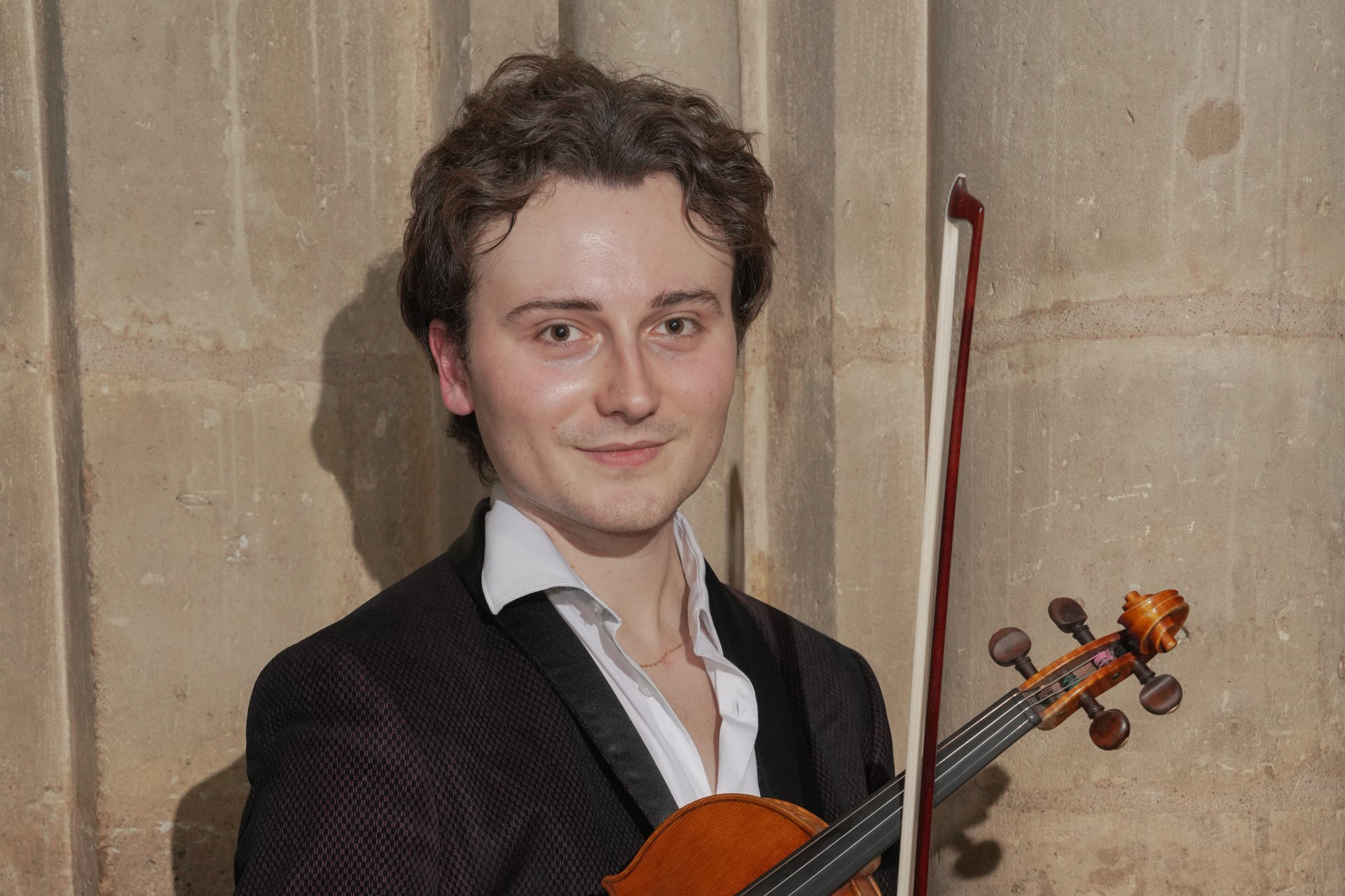 A man in a suit holding a violin under his arm and looking at the camera