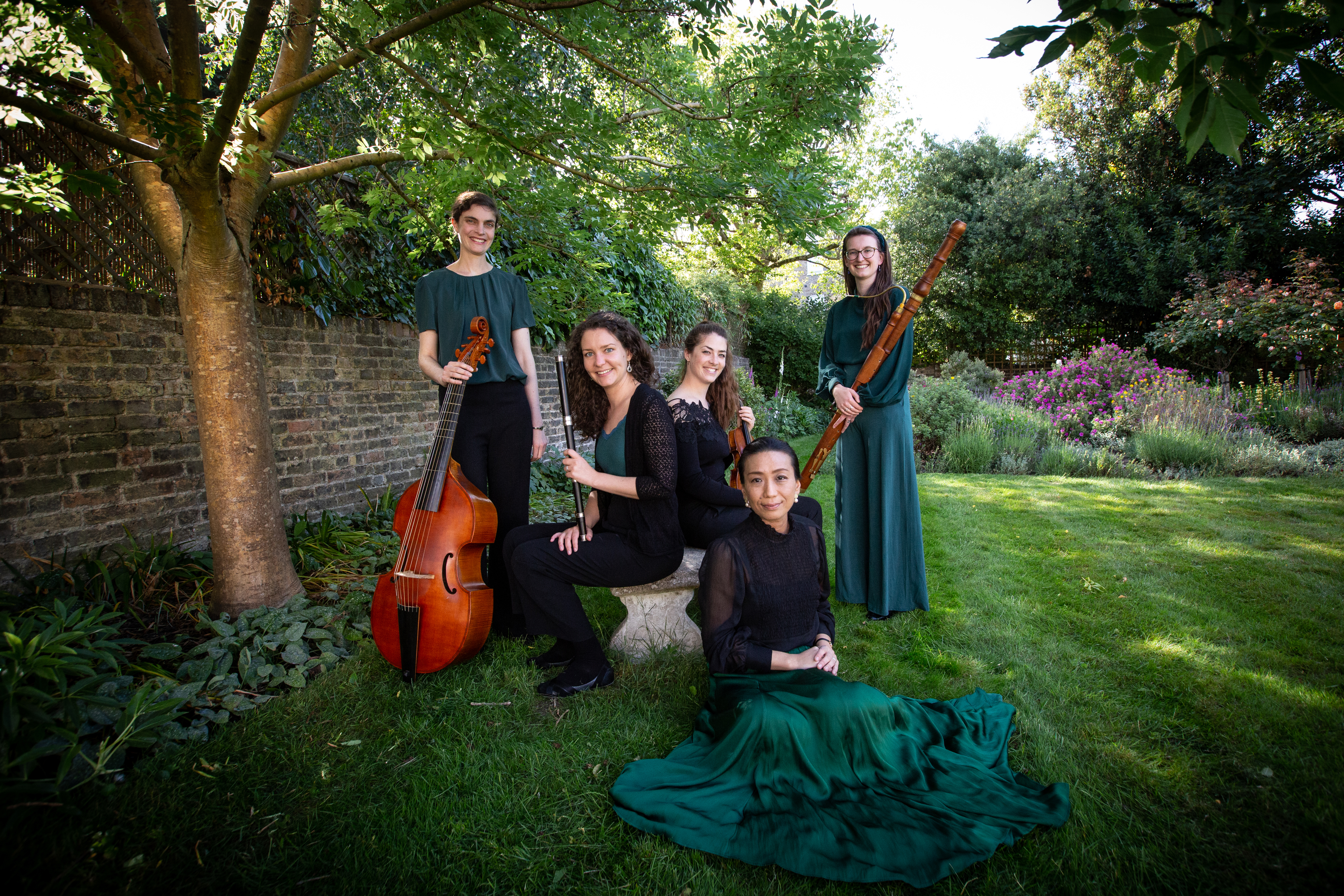 Ensemble Moliere pose with their instruments on the grass of a garden next to a tree
