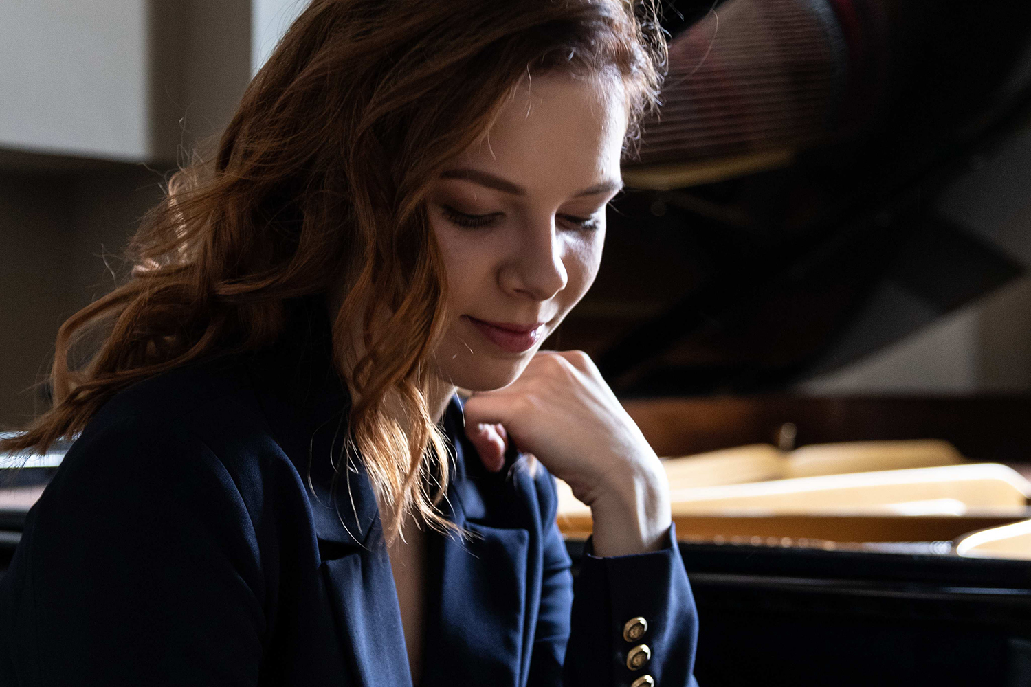 A close up image of a woman looking down sitting next to a grand piano 
