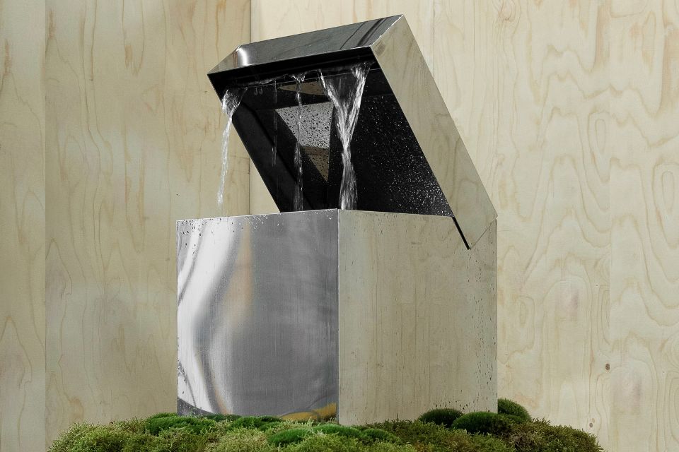 A metal box with an open lid dripping water on a mossy ledge