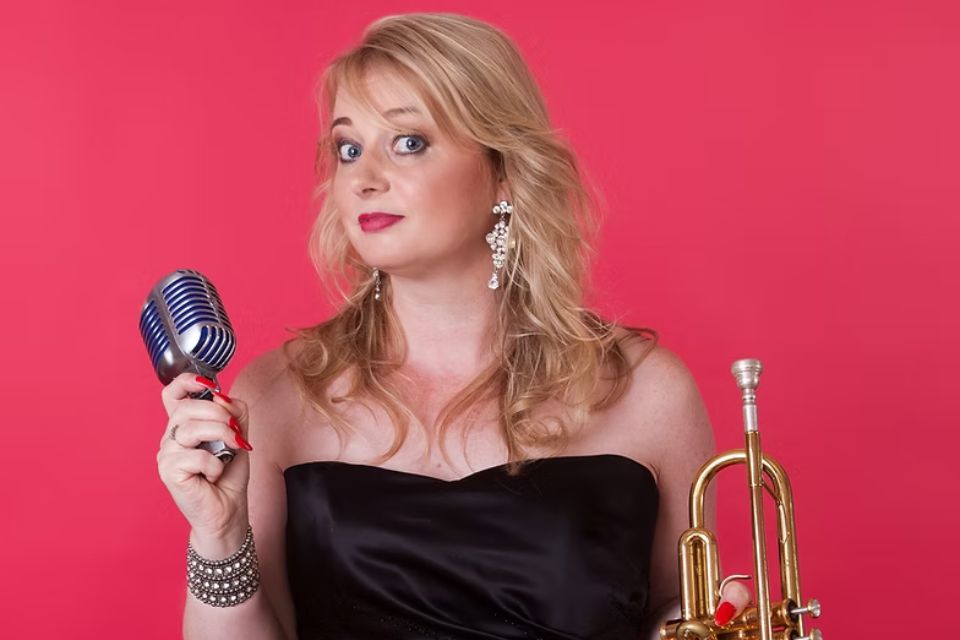 Georgina Jackson holds a trumpet and microphone against a red background