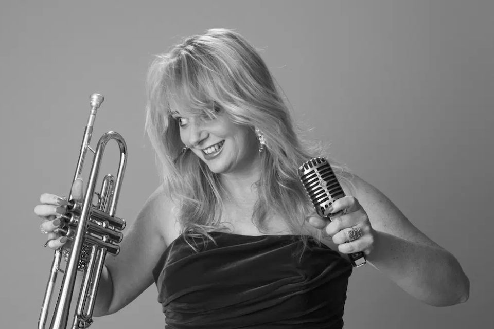 Georgina Jackson holds a trumpet and microphone and smiles