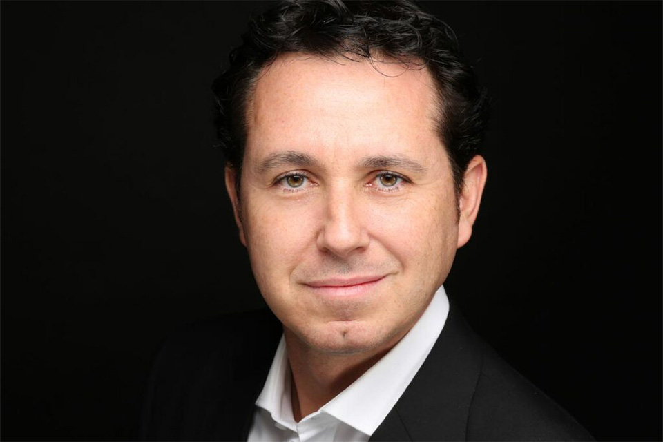 Giuseppe Ravi wears a suit and smiles to camera, against a black background