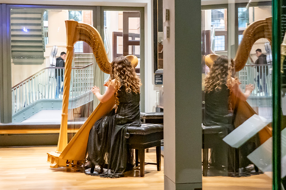 A young woman plays the harp in the RCM Museum