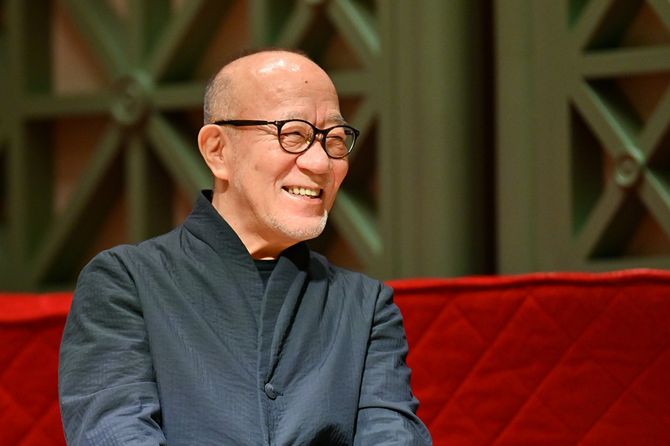 Joe Hisashi wears a black shirt and smiles