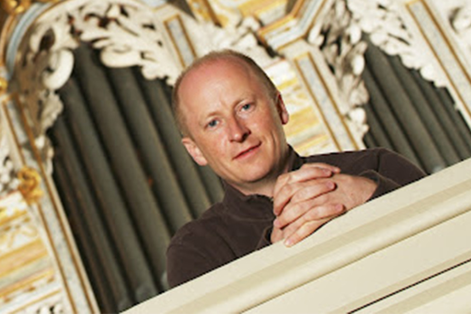An image at an angle: James Johnstone wearing a brown jacket smiles at the camera