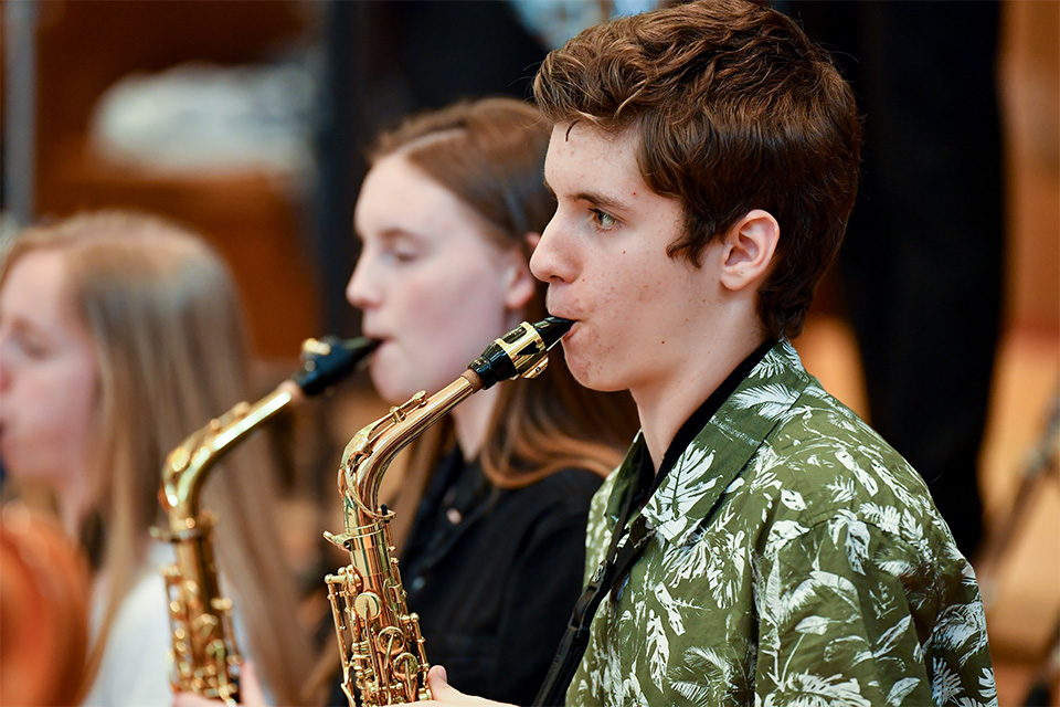 A boy plays his saxophone on stage as part of a wind band