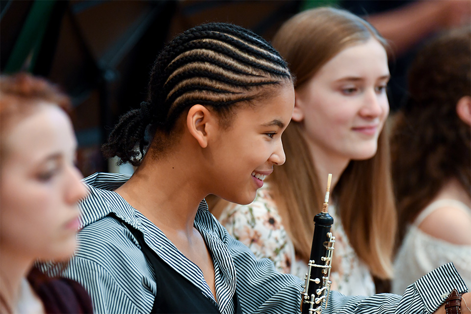 A girl holding an oboe in a orchestra smiles