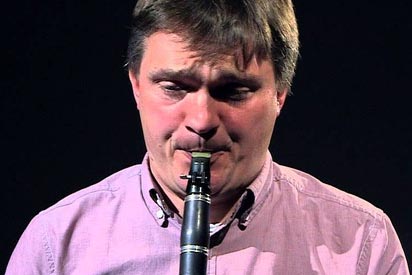 A close up image of a man with a light pink shirt performing on the clarinet