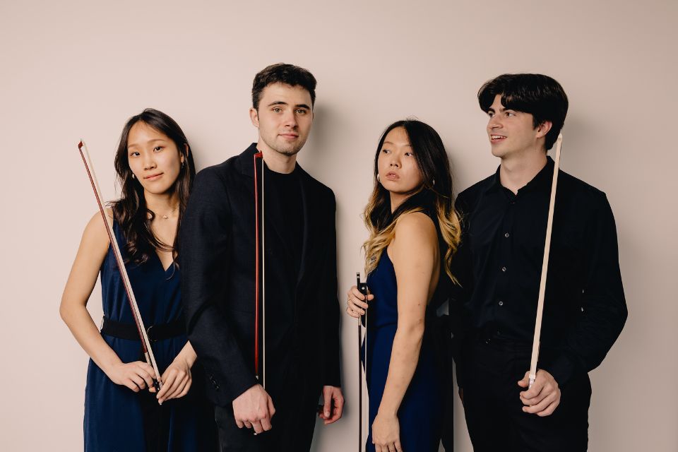 A string quartet performing on stage hold their instruments with their bows in the air
