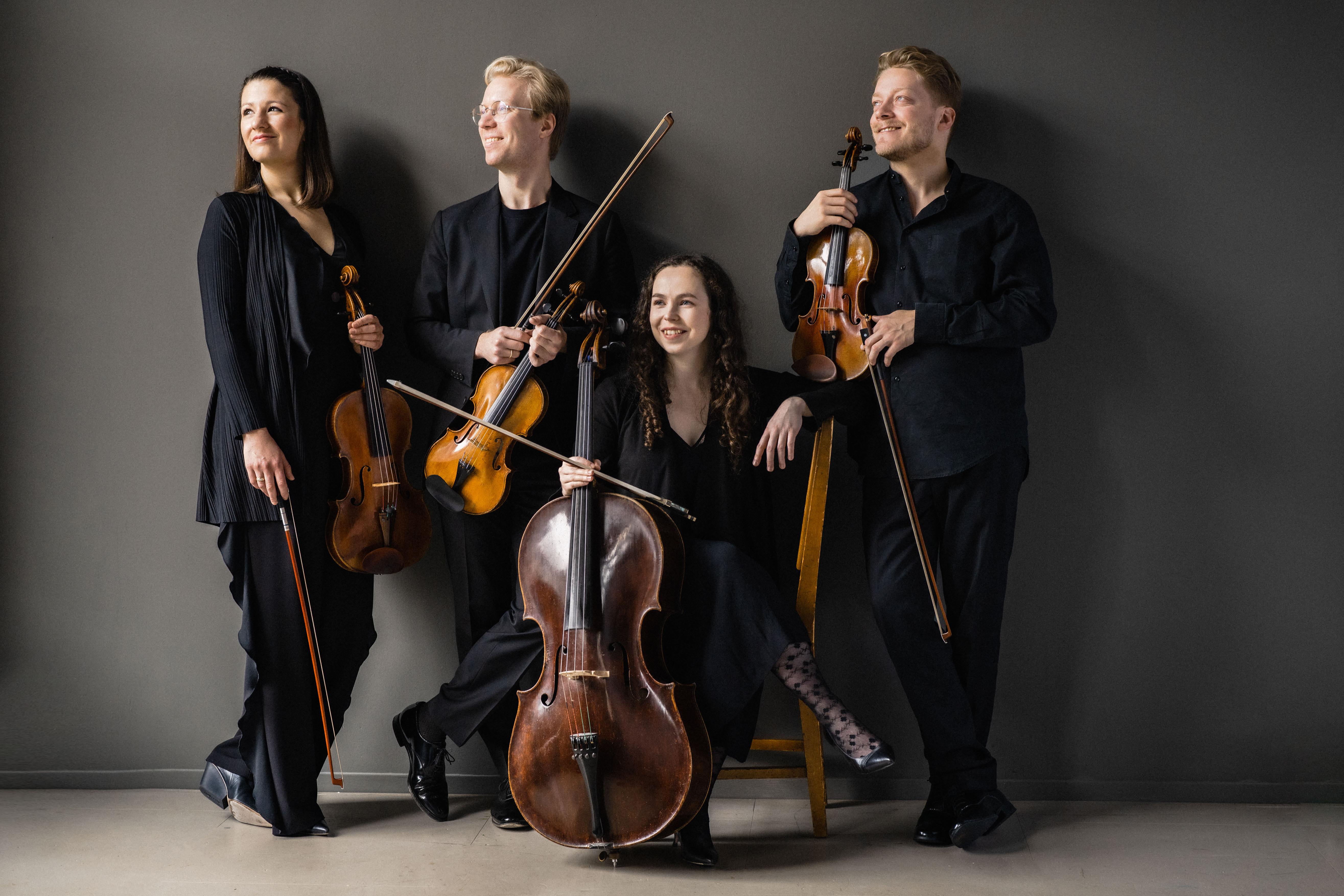Marmen Quartet wearing black, holding their string instruments in a dark grey room and looking off to the side