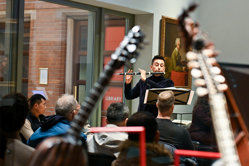 A young man plays the recorder in the RCM Museum surrounded by instruments in display cases