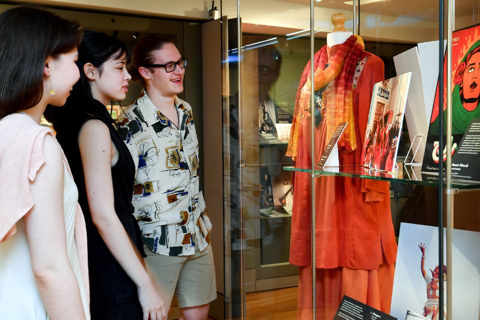 Three people look attentively at a historical musical instrument in a display case