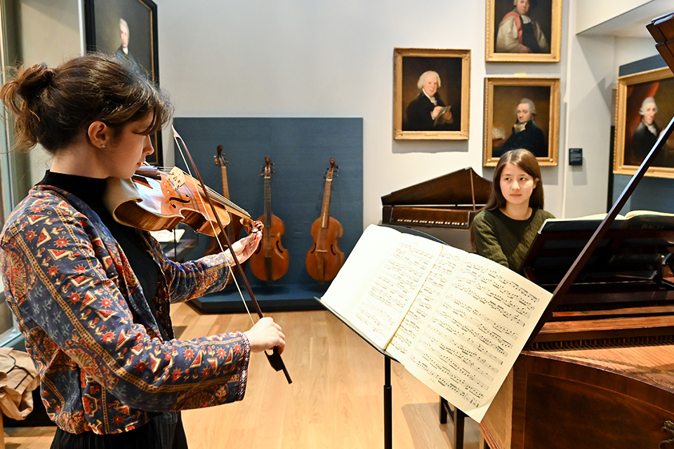 Two students play a harpsichord and a historical violin in the Royal College of Music Museum