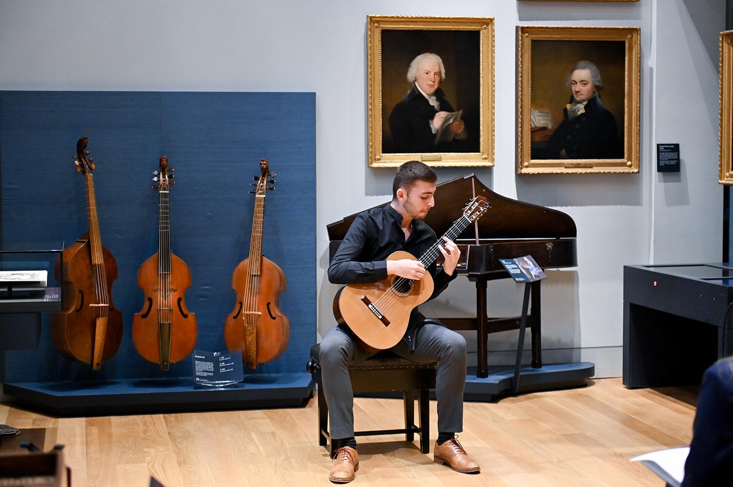 A guitarist wearing black performs in the RCM Museum in front of paintings and historical instruments