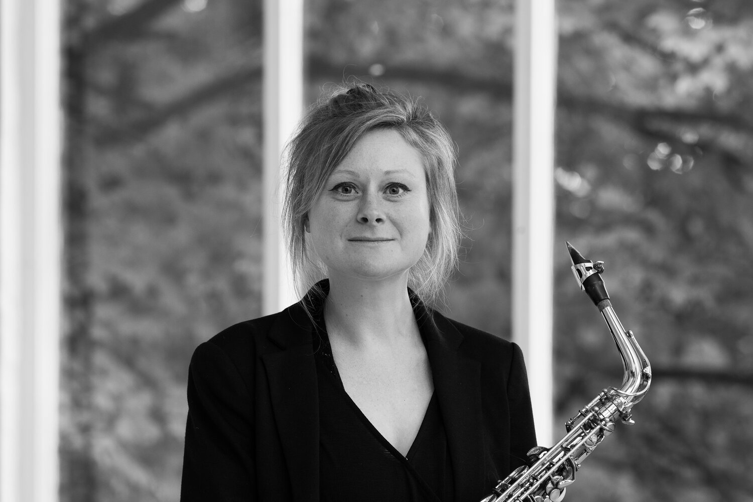 A black and white image of a woman looking into the camera and holding a saxophone