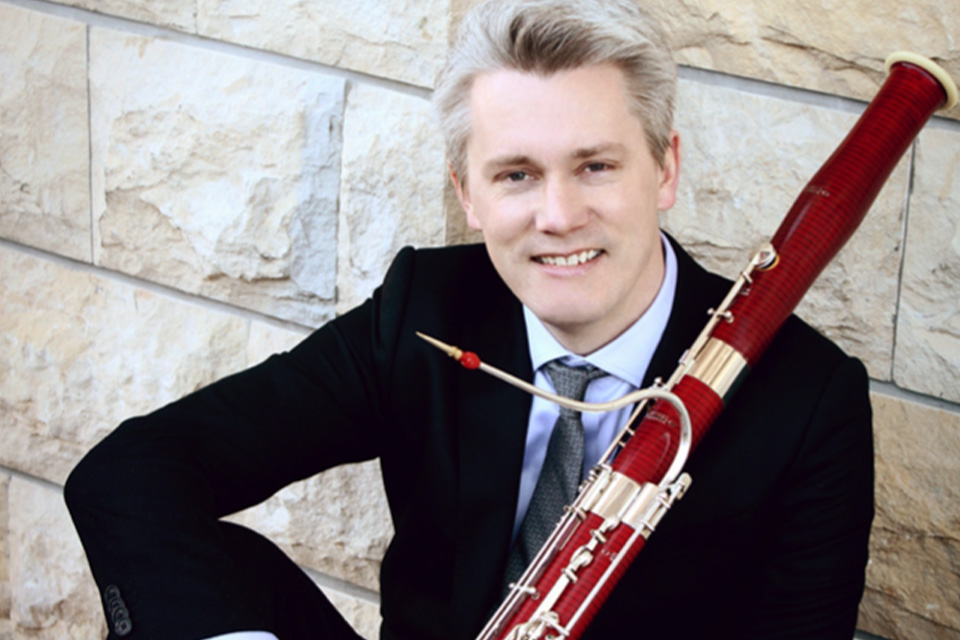 Ole Kristian Dahl leans against a wall holding his bassoon, smiling