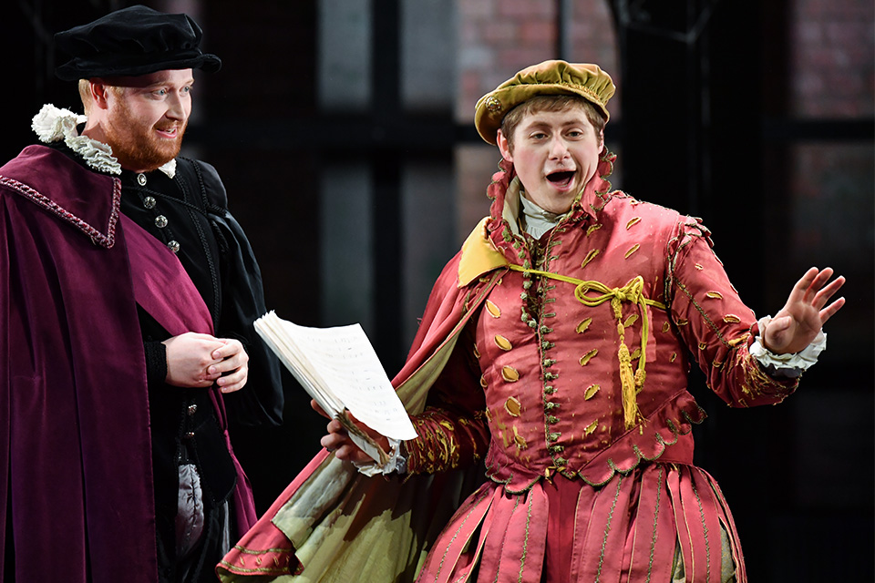 A man in a reinaissance costume sings on stage