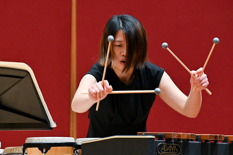 A young woman holds four mallets and performs dramatically