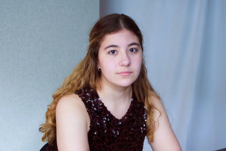 A girl with long hair wears a black top against a pale blue blackground