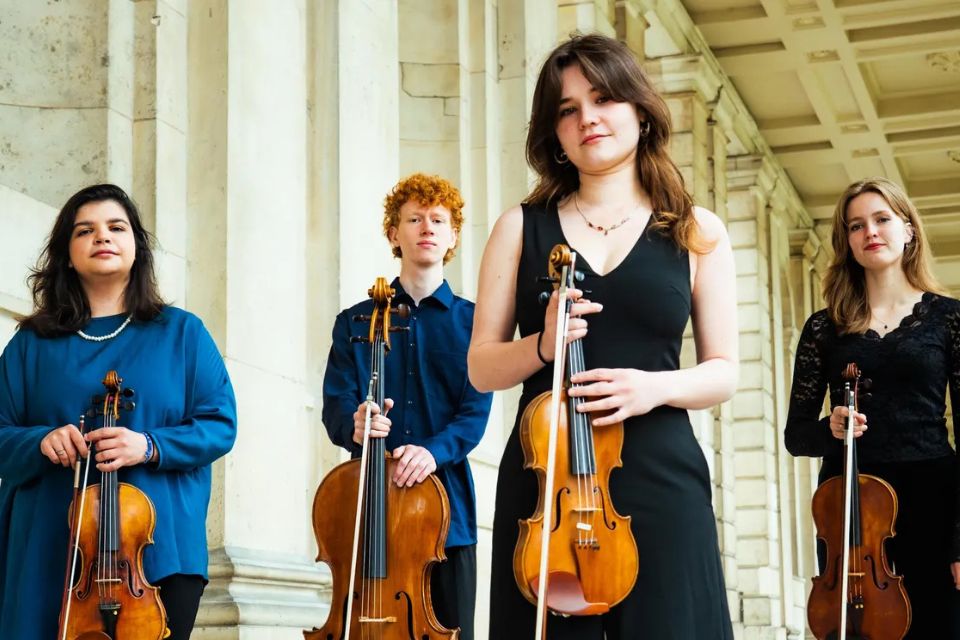 A strings quartet stands in a stone corridor holding their instruments